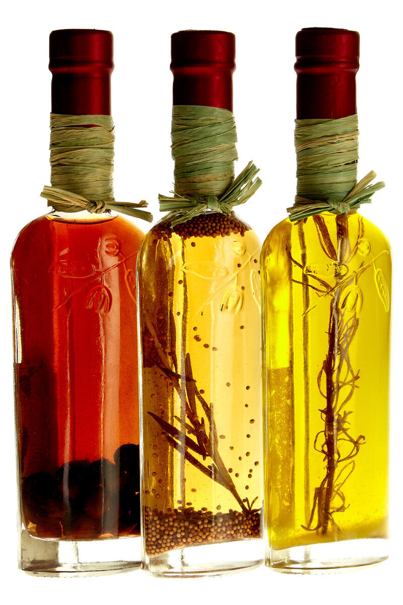 Three bottles of different colored oils with visible ingredients inside, on a white background.