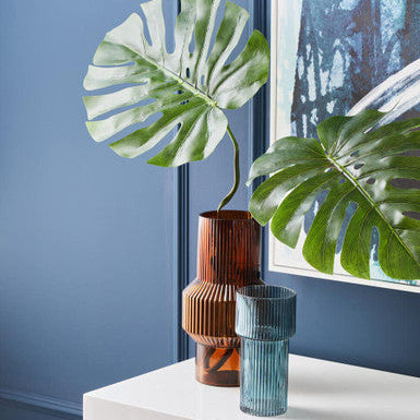 Two vases on a white surface with a blue wall and framed picture in the background