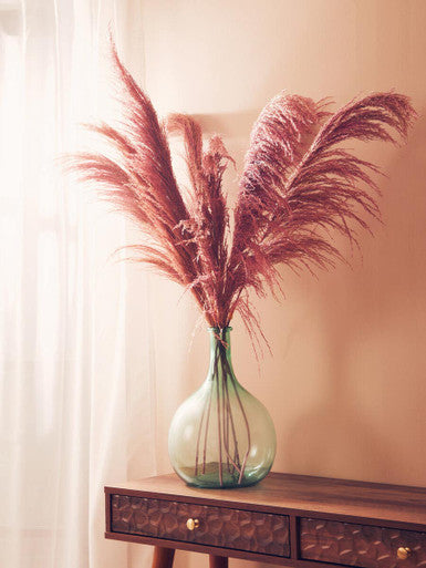 Green vase with dried pampas grass on a wooden console table against a beige wall.