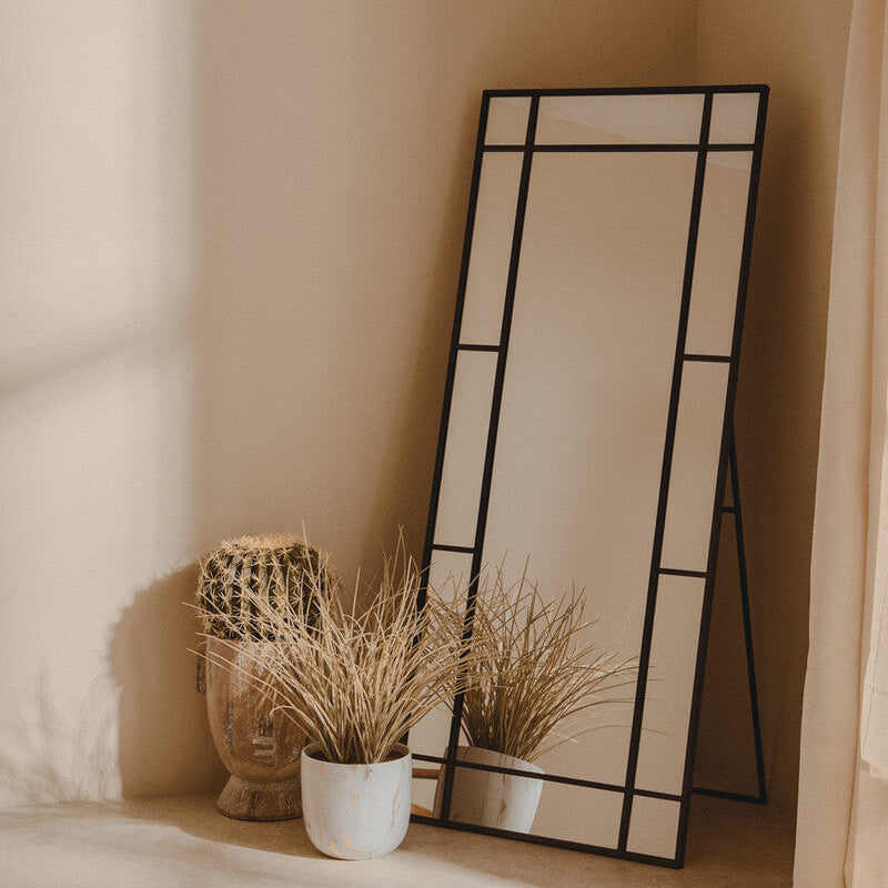 Decorative mirror with geometric design on a beige wall with plants and a vase.