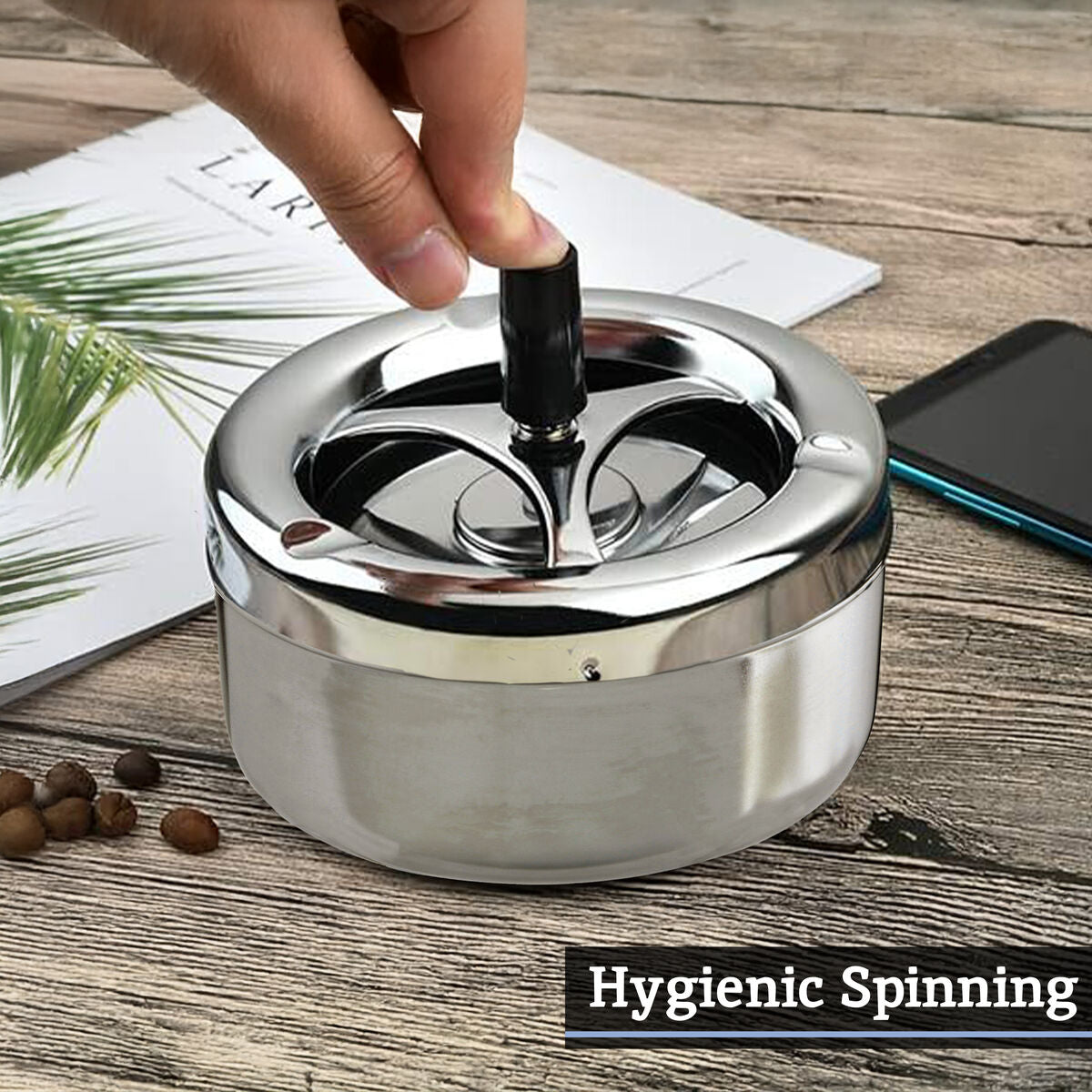 Silver ashtray with a hand spinning it on a wooden surface.