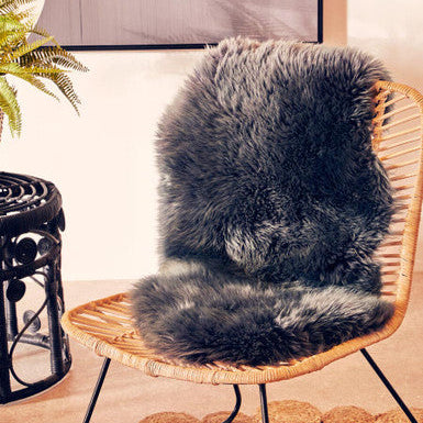 Gray faux fur rug on a wicker chair with a plant and rug in the background