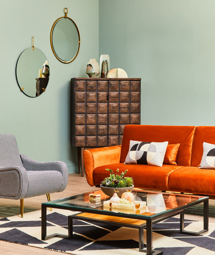 Modern living room with orange sofa, glass coffee table, and decorative elements.