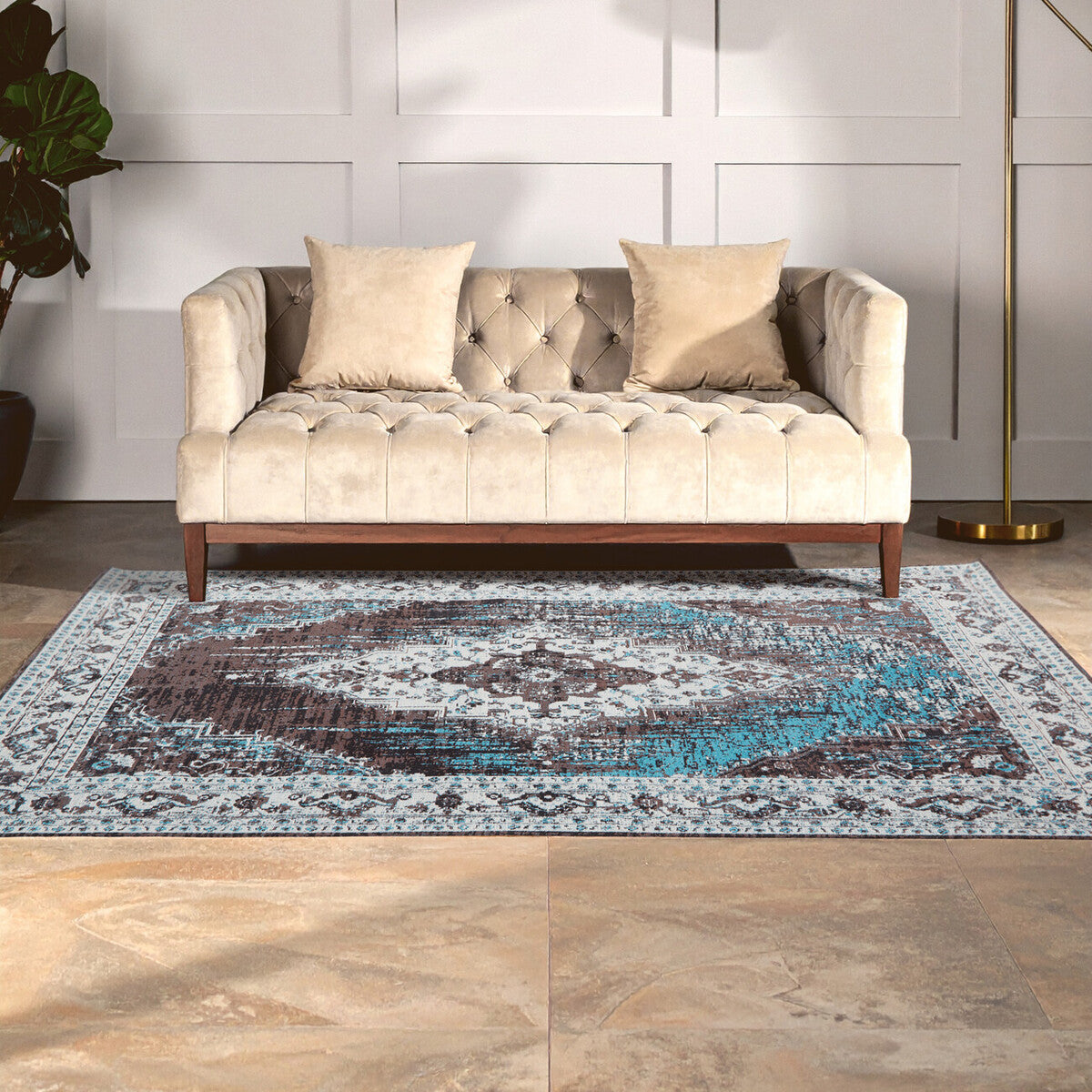 Beige tufted sofa with decorative pillows on a patterned rug in a room with white paneled walls.