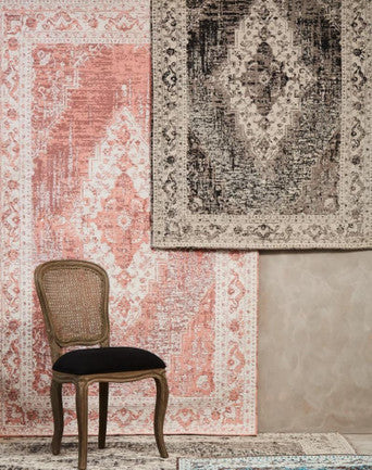 Rugs with intricate patterns on a wall, with a chair in front of one of them.