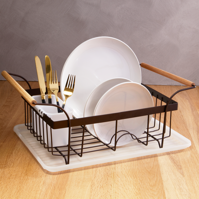 Dish drying rack with plates, cutlery, and a towel on a wooden surface.