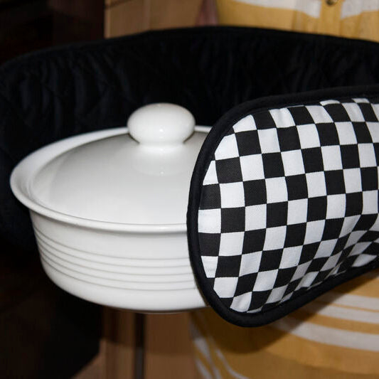 Person holding a white dish with a black and white checkered oven mitt.