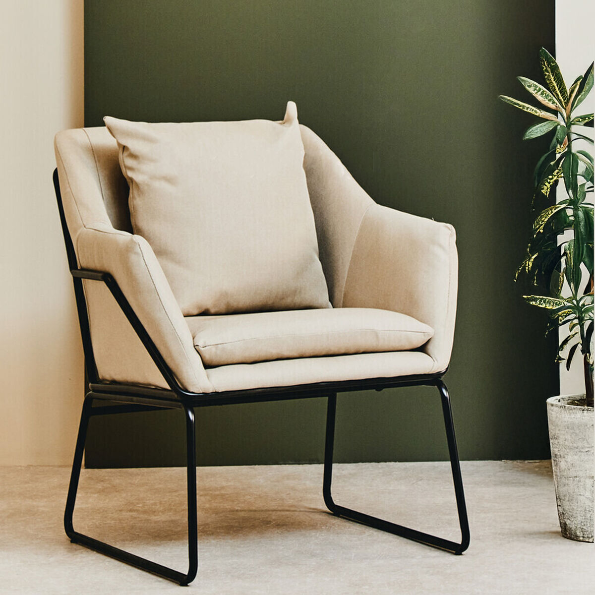 Beige armchair with black metal frame against a green wall