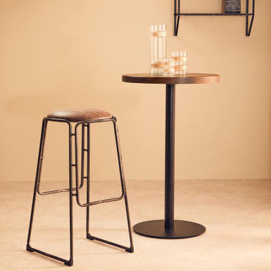 Bar stool and small table against a beige wall with a shelf.