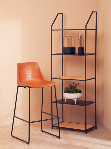 Orange bar stool next to a black metal shelf with decorative items against a beige wall.
