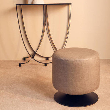 Round beige ottoman in front of a decorative side table with a neutral wall background