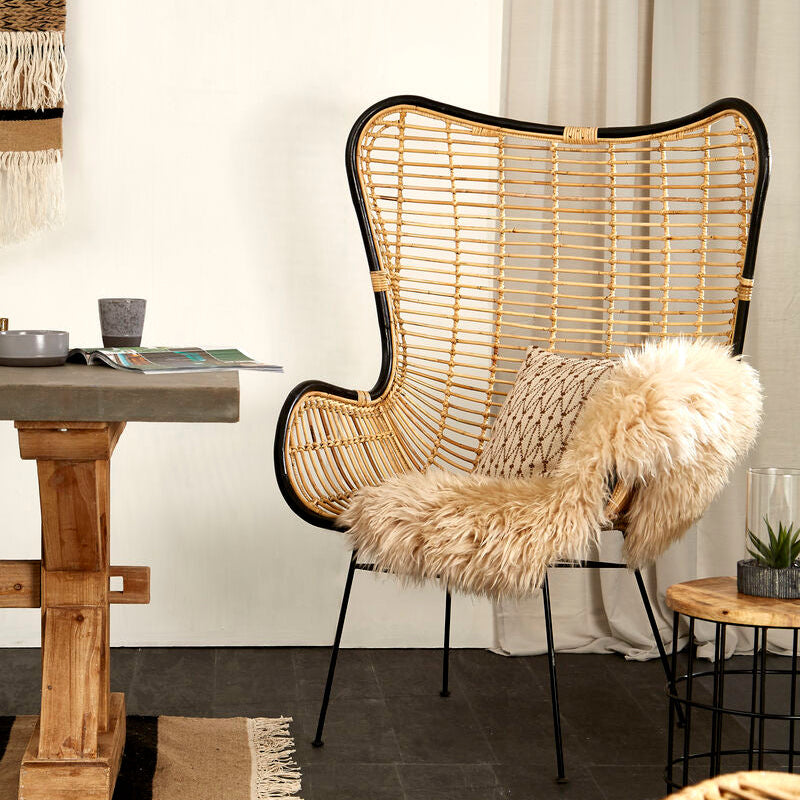 Wicker chair with fur cover in a room with a wooden table and decor items.