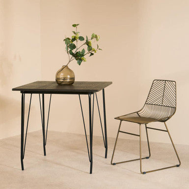 Small table with a vase and plant next to a chair against a beige wall.