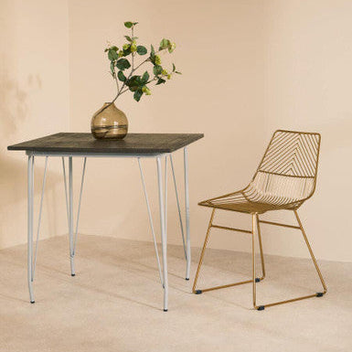 Modern dining table with a vase of flowers and a gold chair against a beige wall.