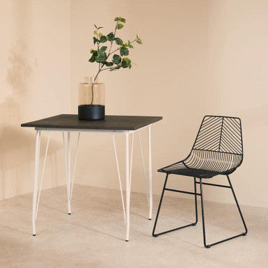 Black dining table with white legs and a black chair against a beige wall.