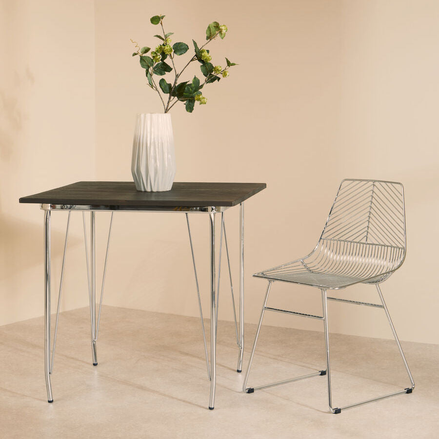 Modern dining table with a vase of flowers and a wire chair against a beige wall.