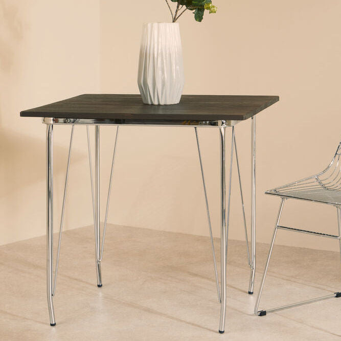 Modern dining table with a vase of flowers and a wire chair against a beige wall.