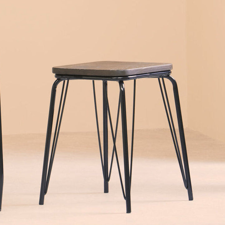 Small black metal stool with a gray cushioned seat against a beige wall.