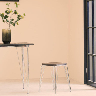 Small table and stool set against a beige wall with a plant on the table.