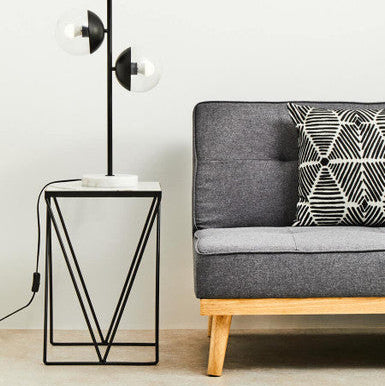 Gray sofa with a geometric pillow next to a modern side table and floor lamp.