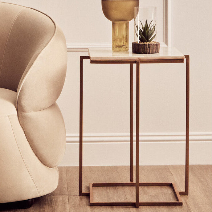 Beige armchair next to a small side table with a decorative item in a minimalistic room.