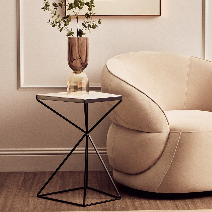 Beige armchair next to a geometric side table with a plant in a room.