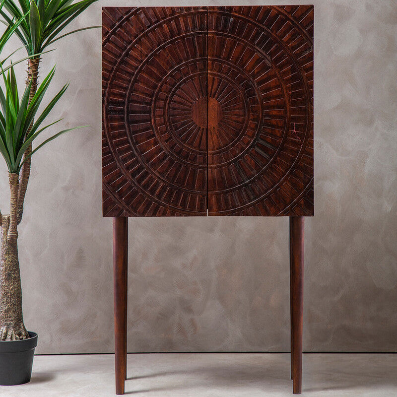 Wooden cabinet with decorative pattern next to a potted plant against a neutral wall.