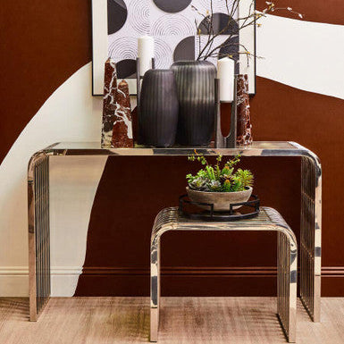 Modern interior with a glass console table, decorative vases, and artwork against a brown wall.
