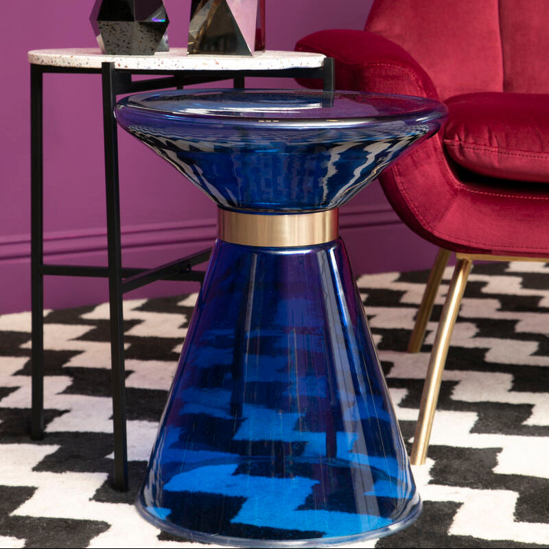 Blue glass table with gold accents in a room with a red chair and purple wall.