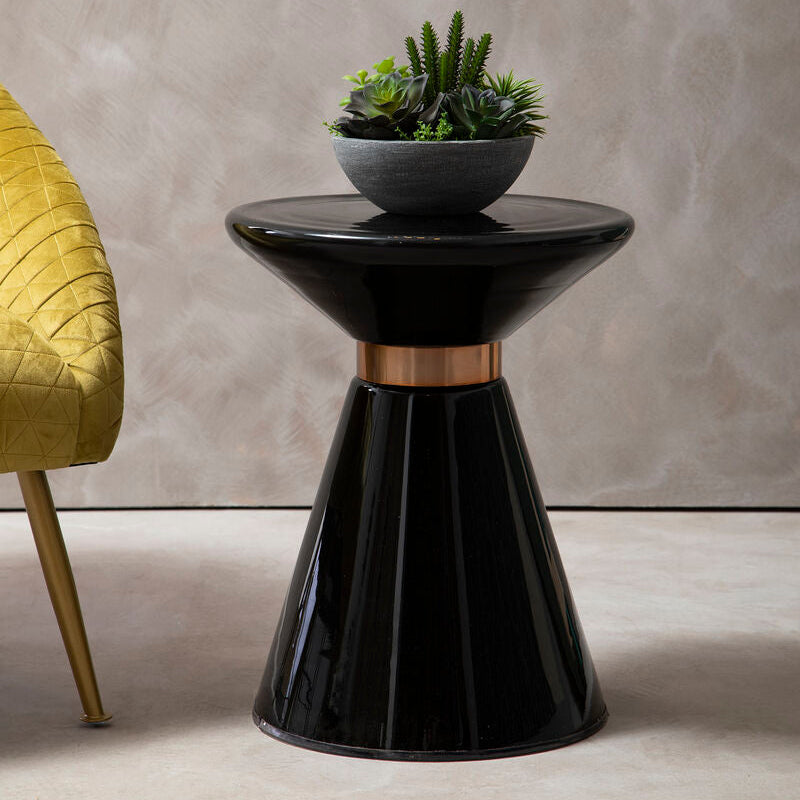 Black side table with a plant on it next to a yellow chair against a gray wall.
