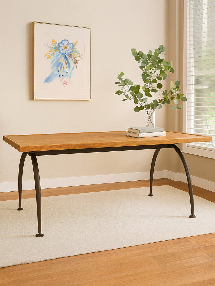 Wooden desk with metal legs in a room with a painting and plant on the wall.