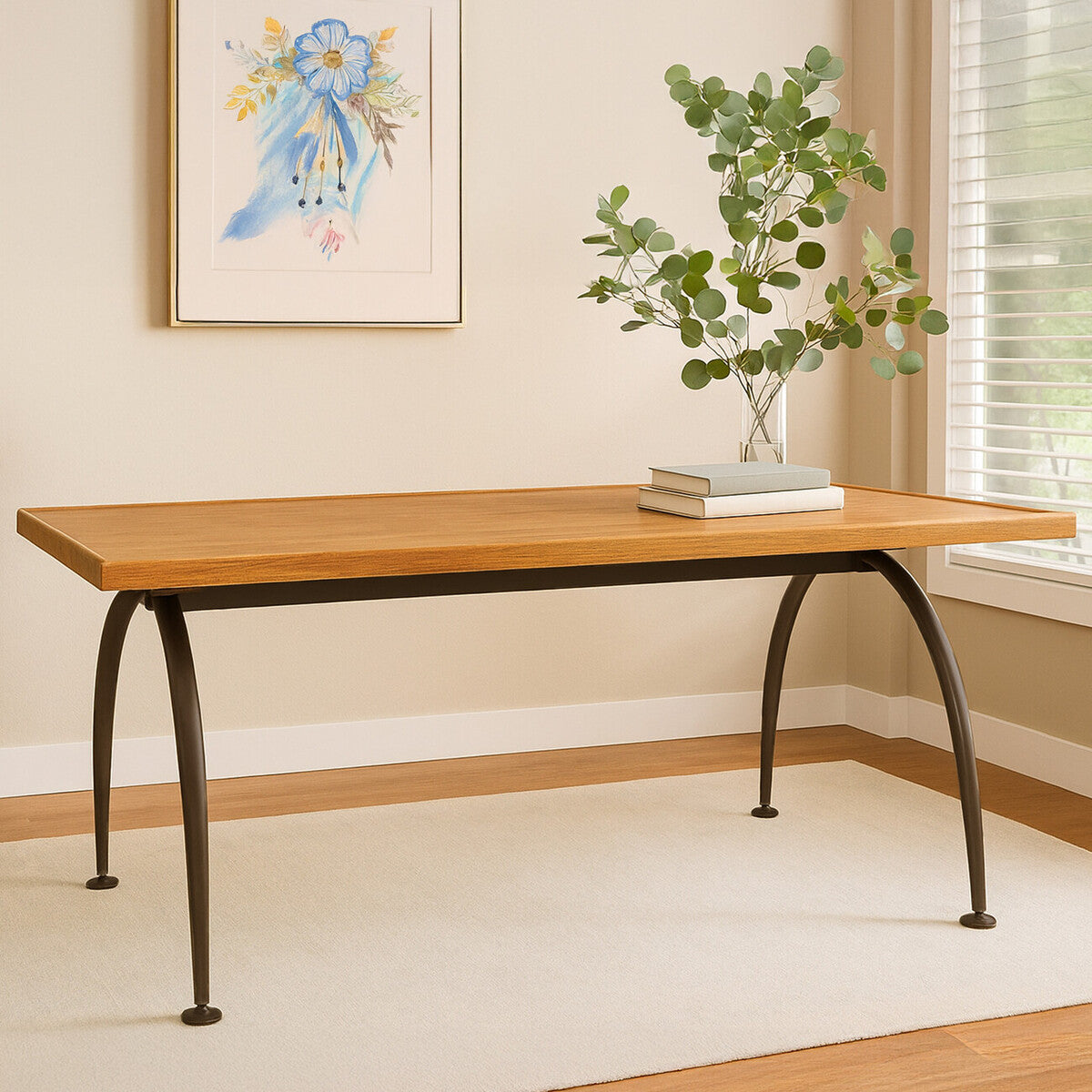 Wooden table with metal legs in a room with a painting and plant on the wall.