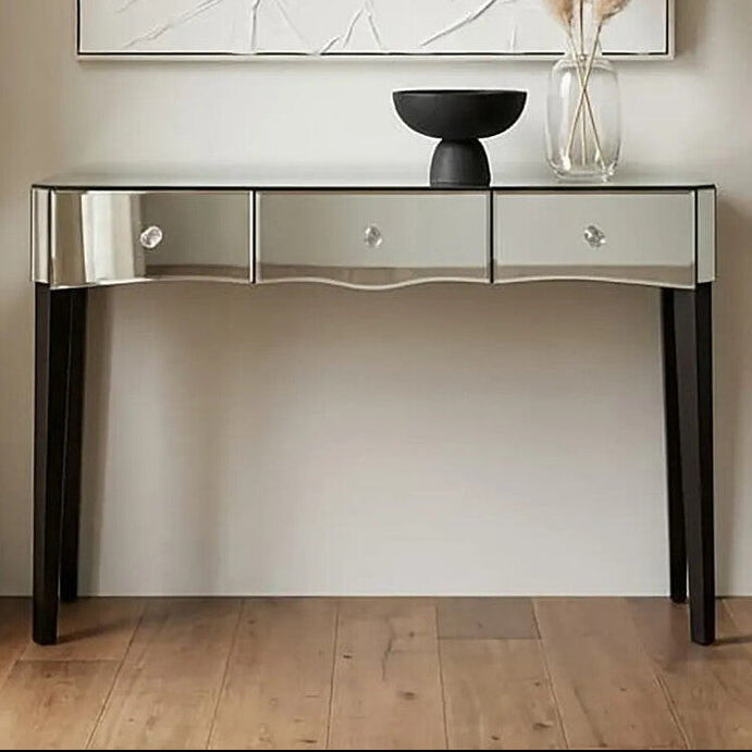 Decorative console table with a mirror finish against a neutral wall with abstract art and pampas grass.