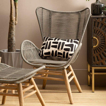 Wicker chair with a patterned pillow in a room with a plant and decorative cabinet.