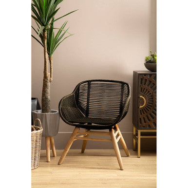 Black woven armchair in a room with a plant and decorative items.