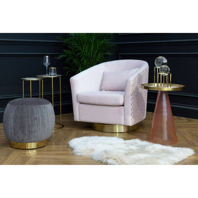 Modern living room setup with a pink armchair, gray ottoman, and gold side tables.