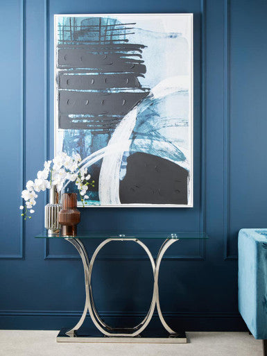 Abstract art piece on a blue wall with a decorative console table and flowers.
