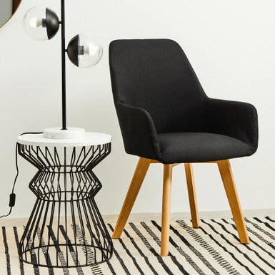 Black chair and wire side table on a patterned rug with a white wall background