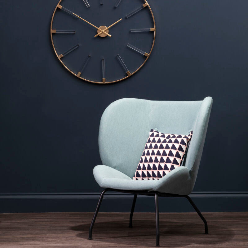 Light blue armchair with a patterned pillow against a dark blue wall with a large clock.