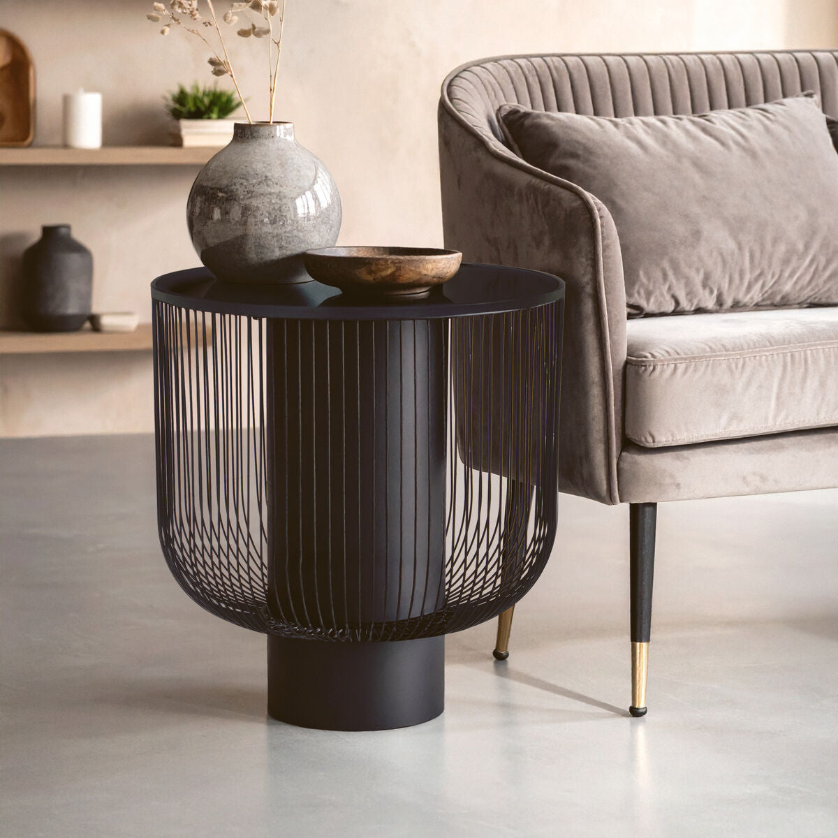 Black wire side table in a living room setting with a sofa and decorative items.