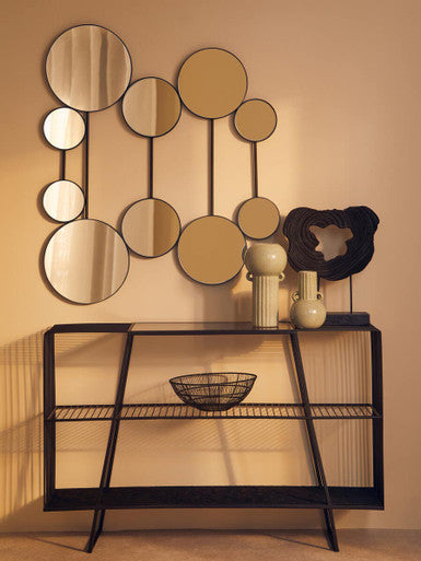 Decorative wall mirror with round mirrors and a black console table against a beige wall.