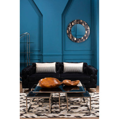 Modern living room with a black sofa, wooden coffee table, and decorative mirror against a blue wall.