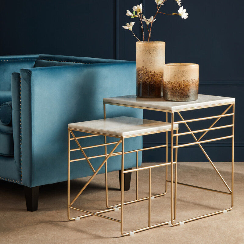 Gold side table with marble top next to a blue armchair against a dark wall.