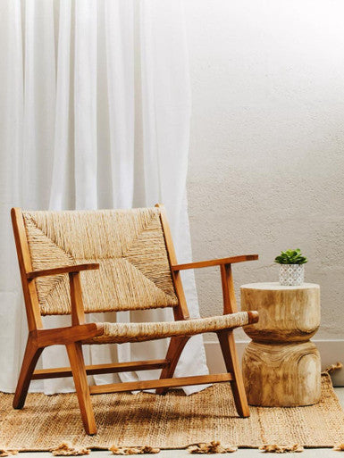 Wooden armchair with woven backrest in a room with white curtains and a small table.