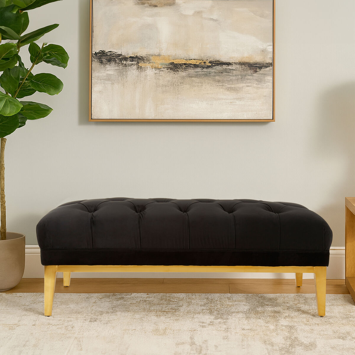 Black tufted bench with wooden legs in a room with abstract art and plant.