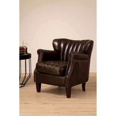 Brown leather armchair in a room with a beige wall and wooden floor.