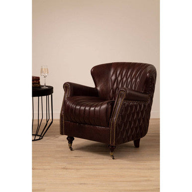 Brown leather armchair in a room with a beige wall and wooden floor.