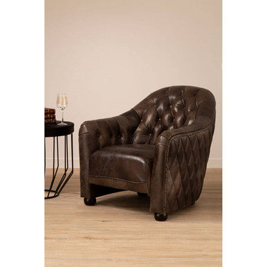 Brown leather armchair in a room with a beige wall and wooden floor.
