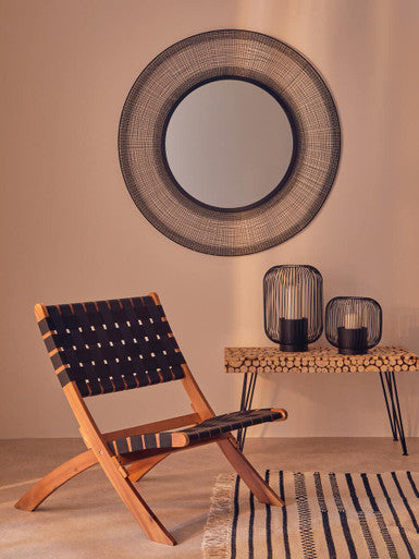 Round woven mirror above a chair with a side table and decorative items in a room.