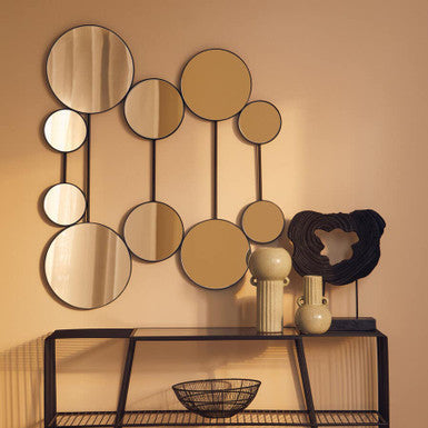 Decorative wall mirror with round mirrors and a black console table against a beige wall.